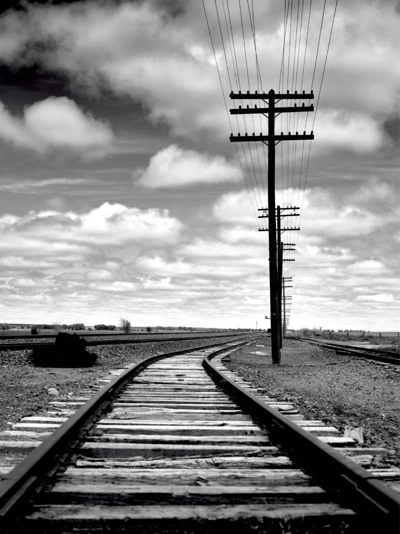 photo of a power line next to a railroad trailing off into the horizon