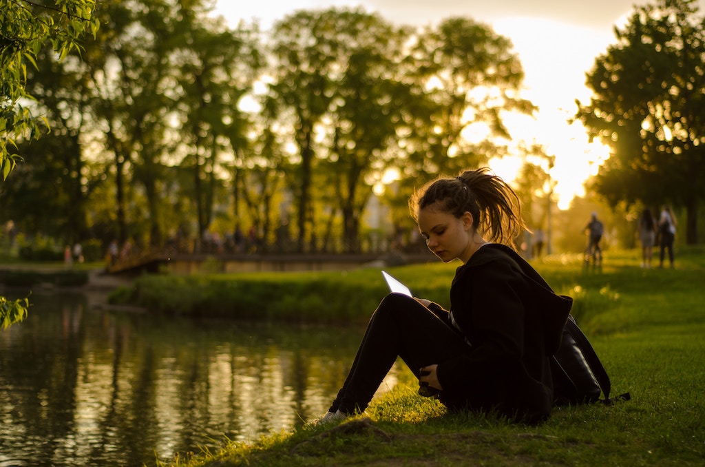 woman sitting on grass field beside body of water during golden hour. Photo by Vadim Fomenok on Unsplash